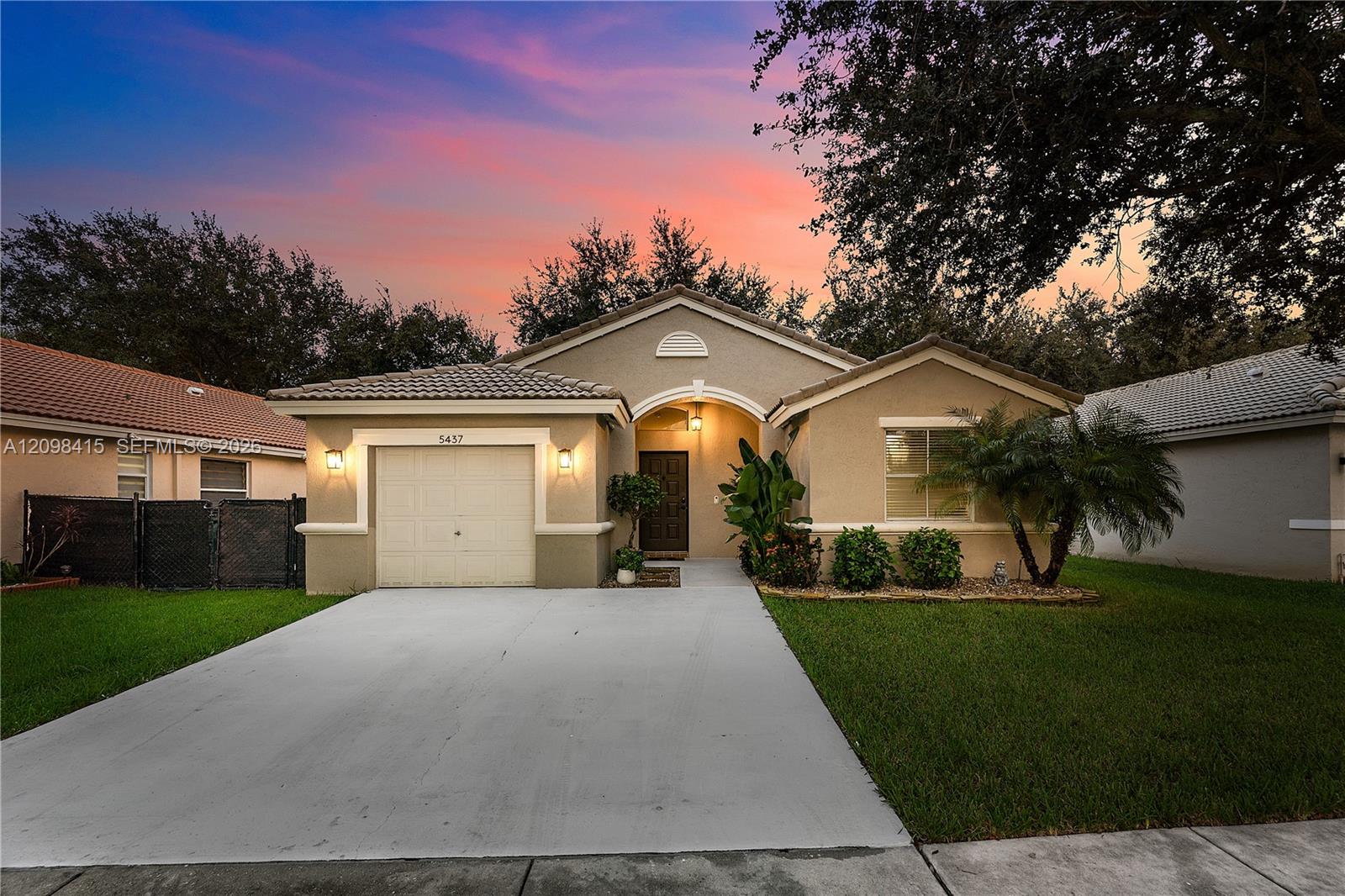 Single-story stucco home with an attached garage and wide driveway beneath a colorful dusk sky.