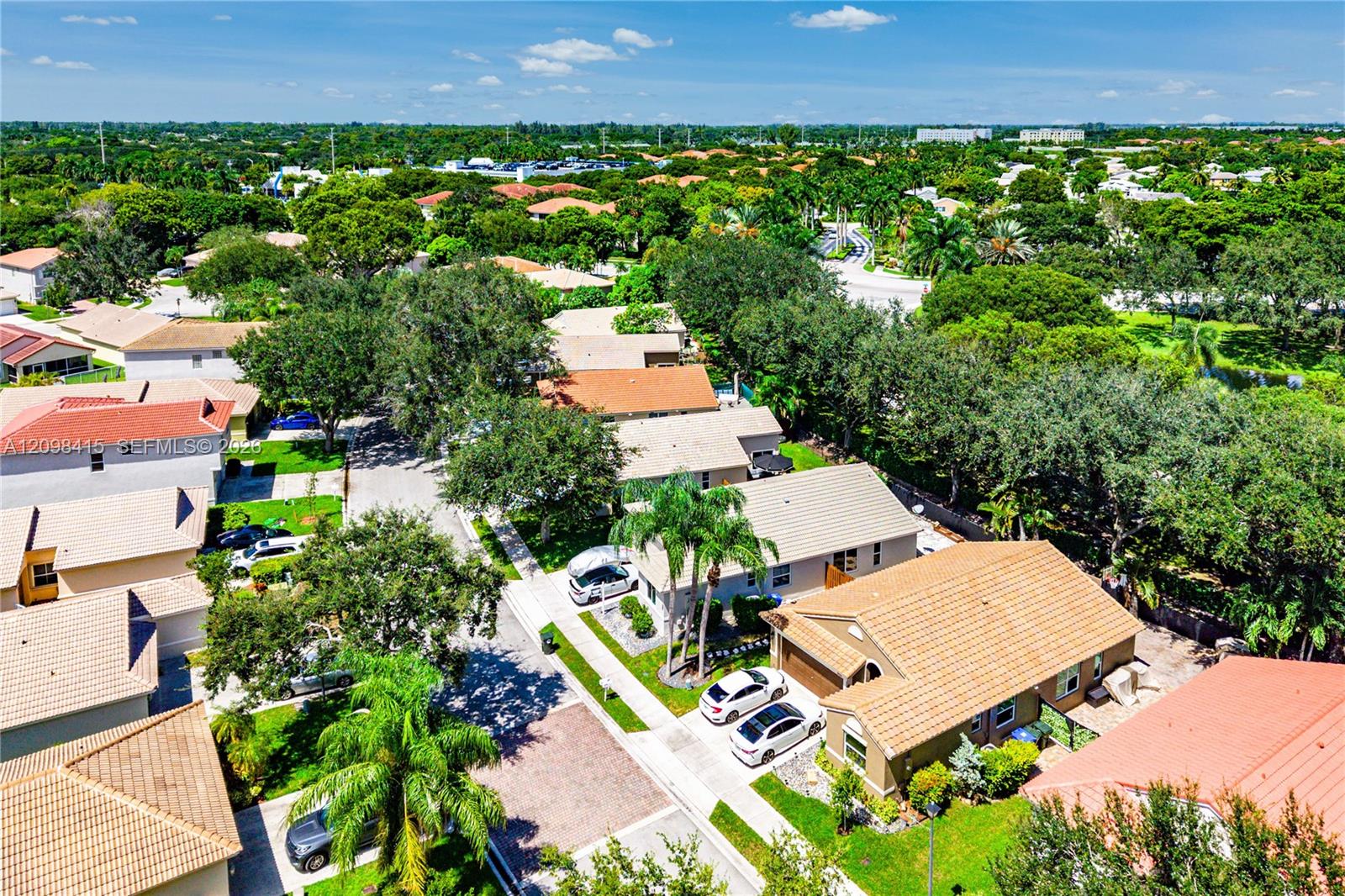 Aerial view of a leafy neighborhood with tile-roofed homes, palm trees, and winding streets.
