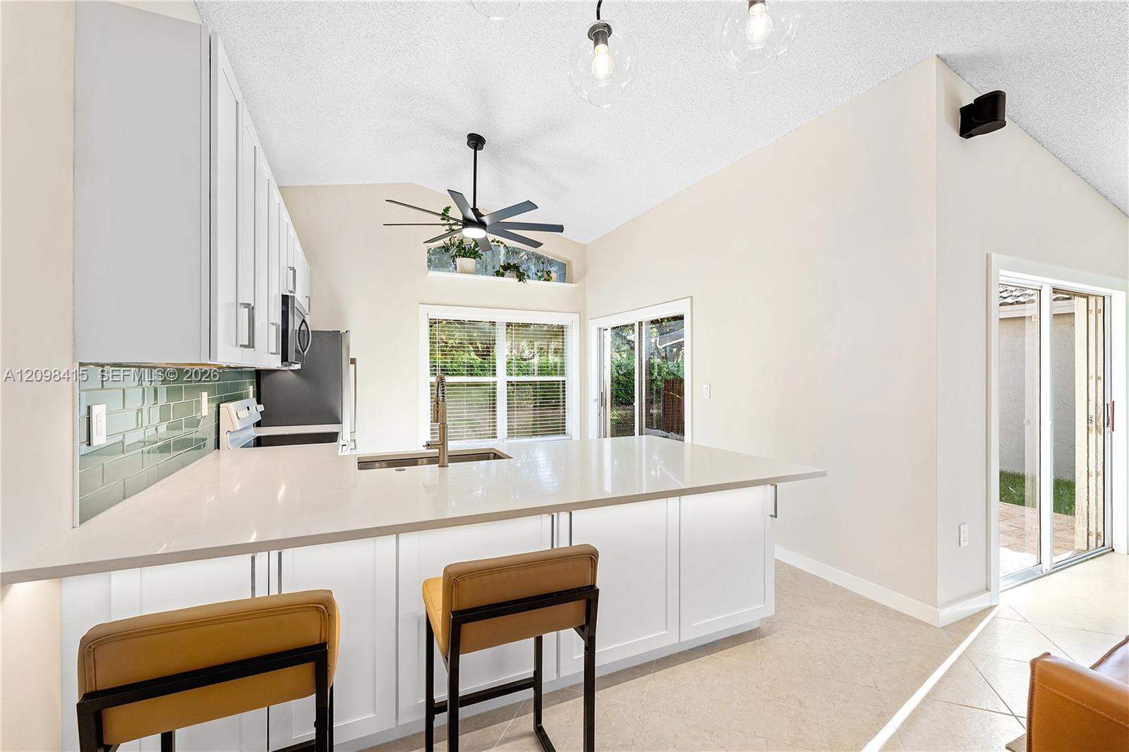 Bright kitchen with a large island, white cabinets, pale green tile backsplash, and vaulted ceiling.
