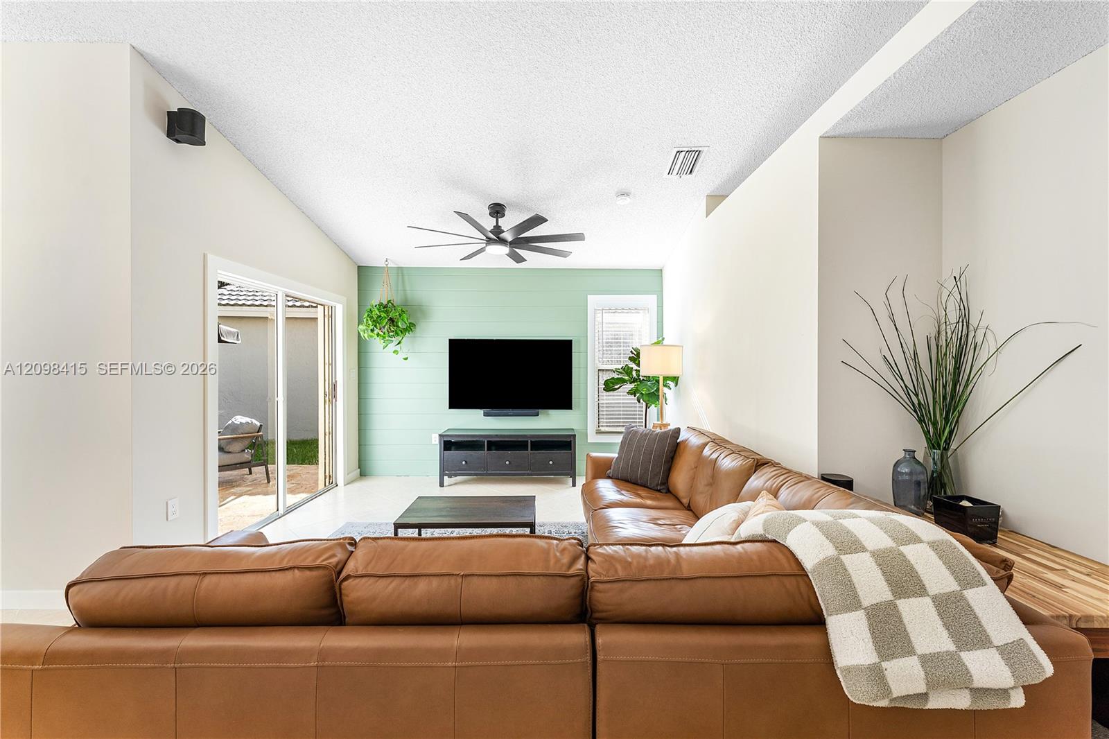 Living room with a brown leather sectional facing a television on a mint-green accent wall.