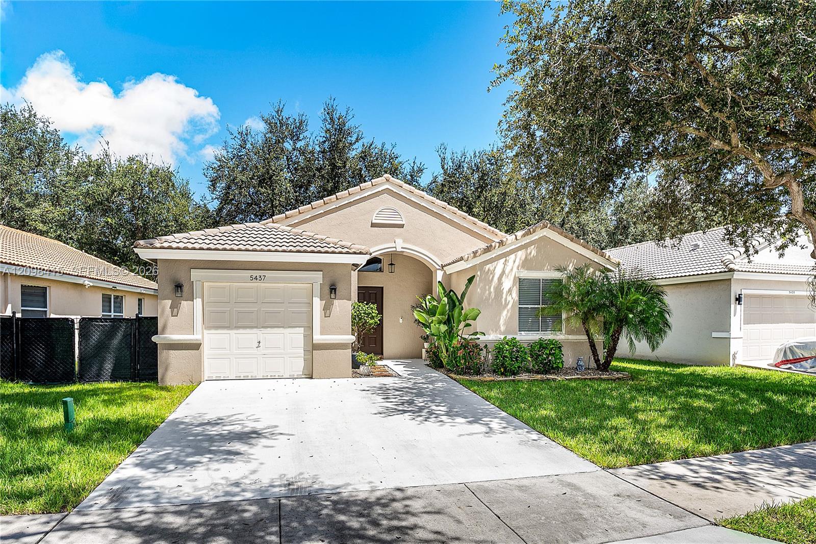 Single-story beige stucco home with a tile roof, attached garage, and tropical landscaping.