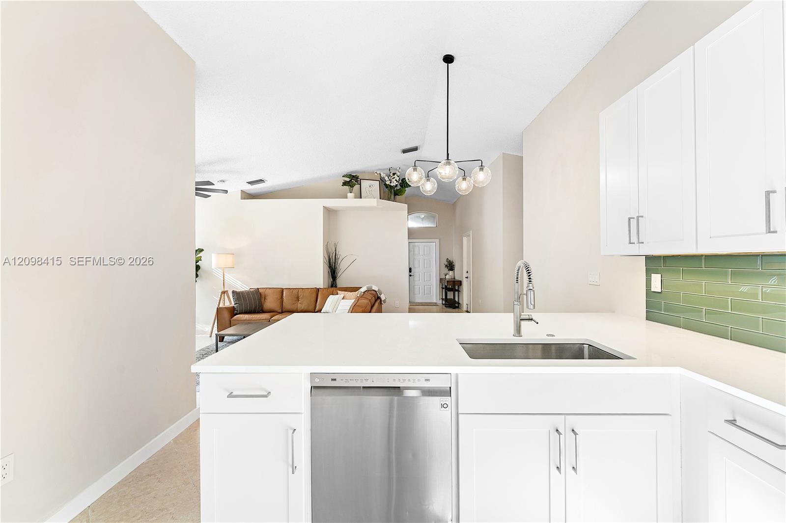 Open-plan kitchen with white cabinetry, green tile backsplash, and a view into the living room.