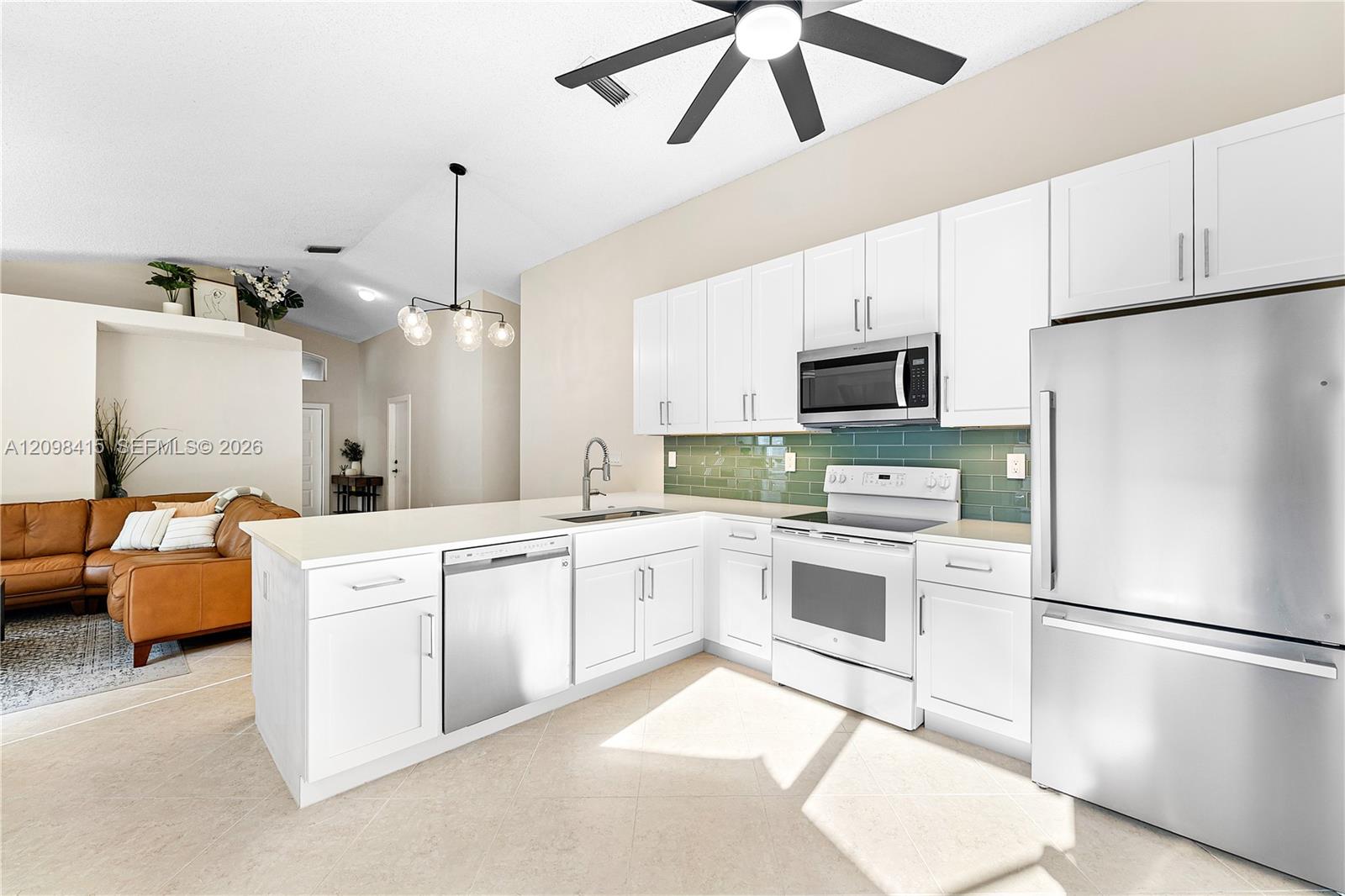 Open kitchen with white cabinets, green tile backsplash, stainless appliances, and an island beside a tan sofa.