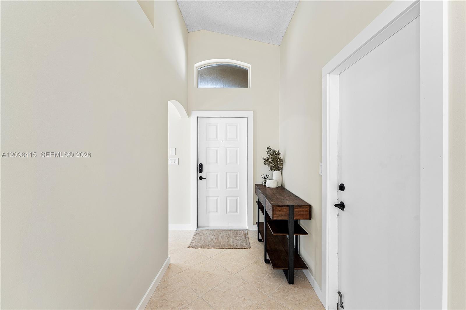 Entry foyer with a white front door, arched window, tiled floor, and dark wood console table.