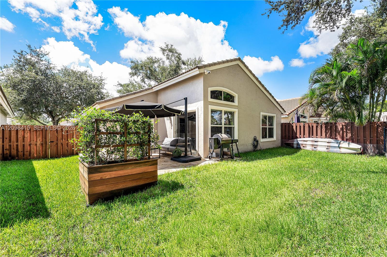 Backyard of a beige single-story home with a patio, raised planter, grill, and hot tub.