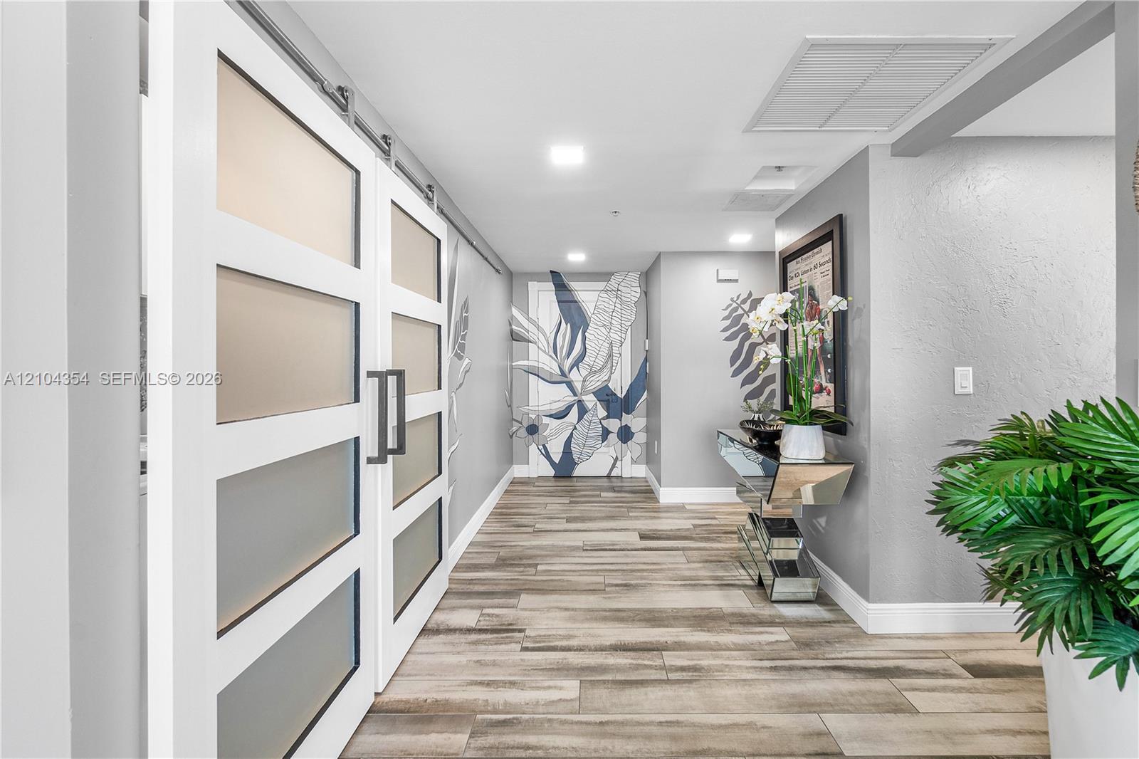 Apartment hallway with frosted-panel sliding doors, wood-look tile flooring, and a mirrored console table.