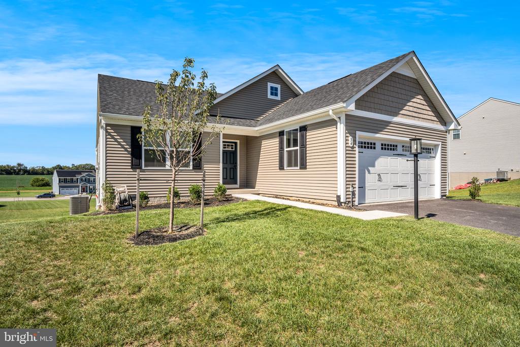 Beige single-story house with an attached two-car garage and young trees in the front lawn.