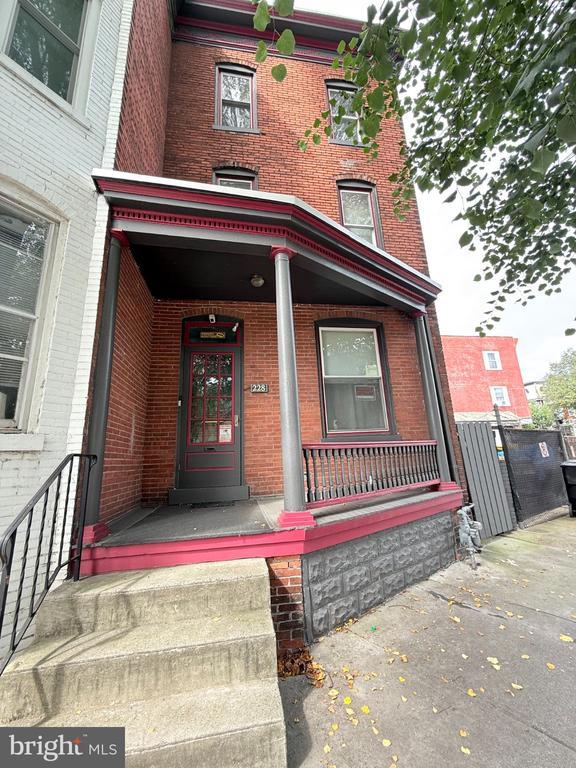 Red brick rowhouse with a covered porch, red trim, and concrete front steps.