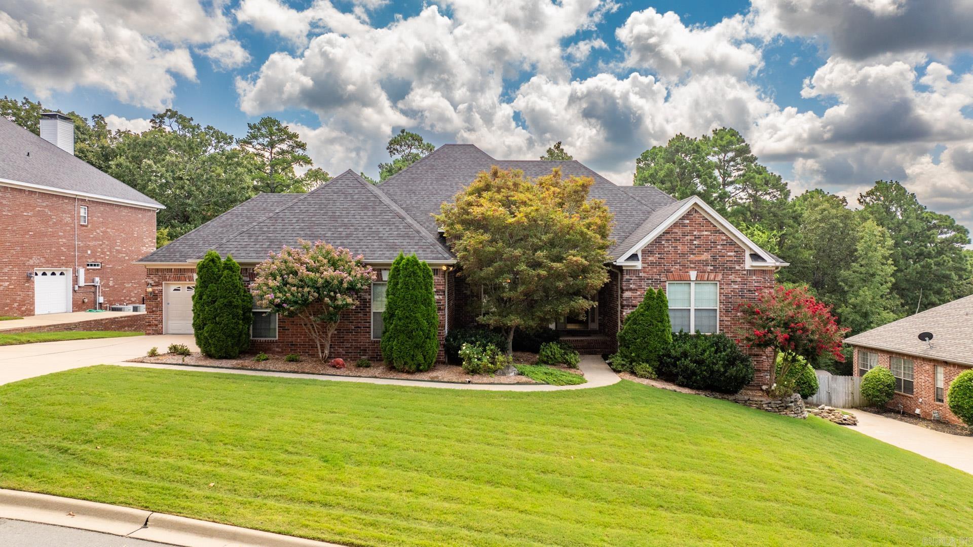 Red brick house with a multi-gabled roof, landscaped shrubs, and a broad front lawn.