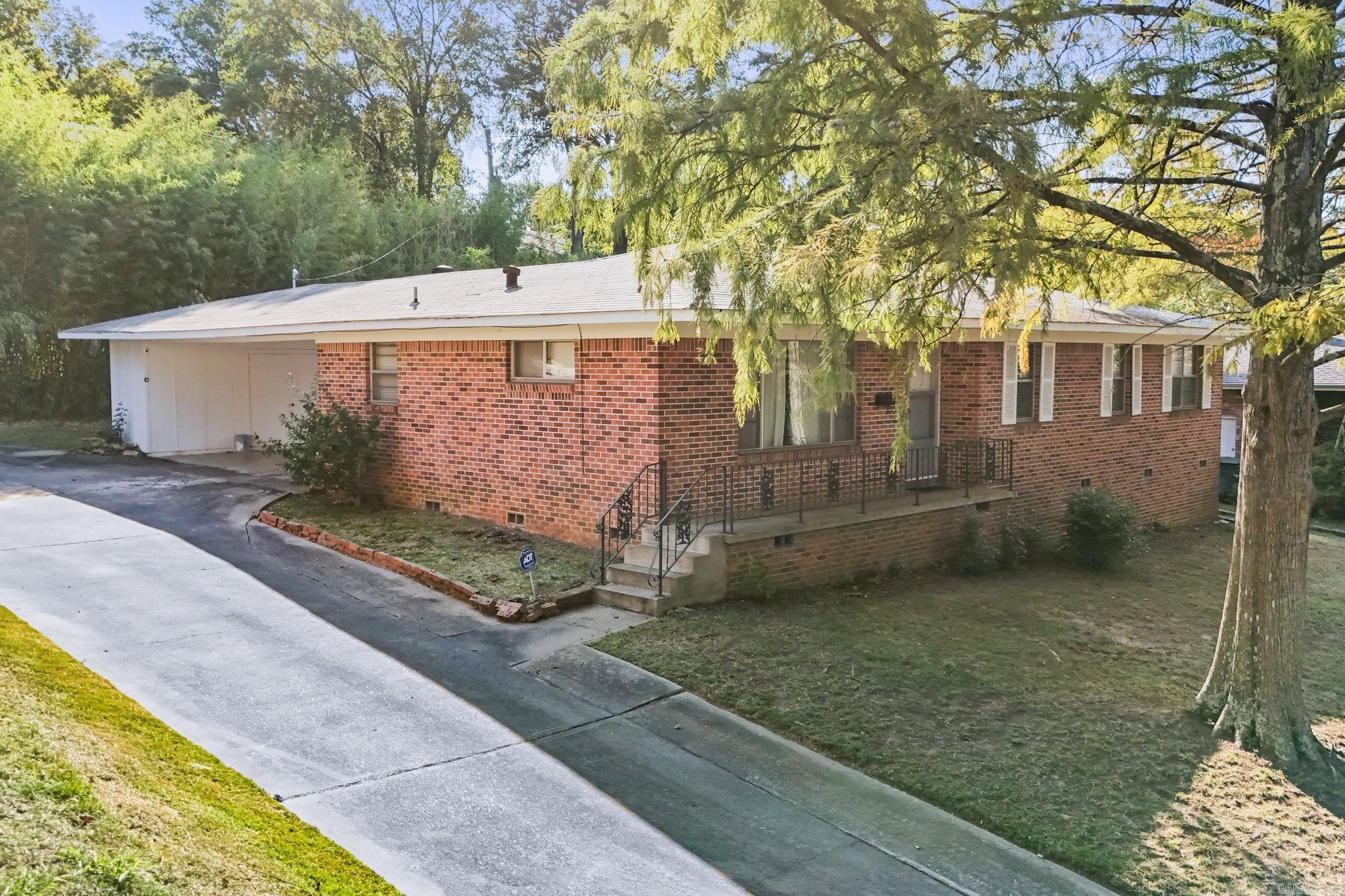 Single-story red brick home with an attached garage, raised porch, and mature trees.