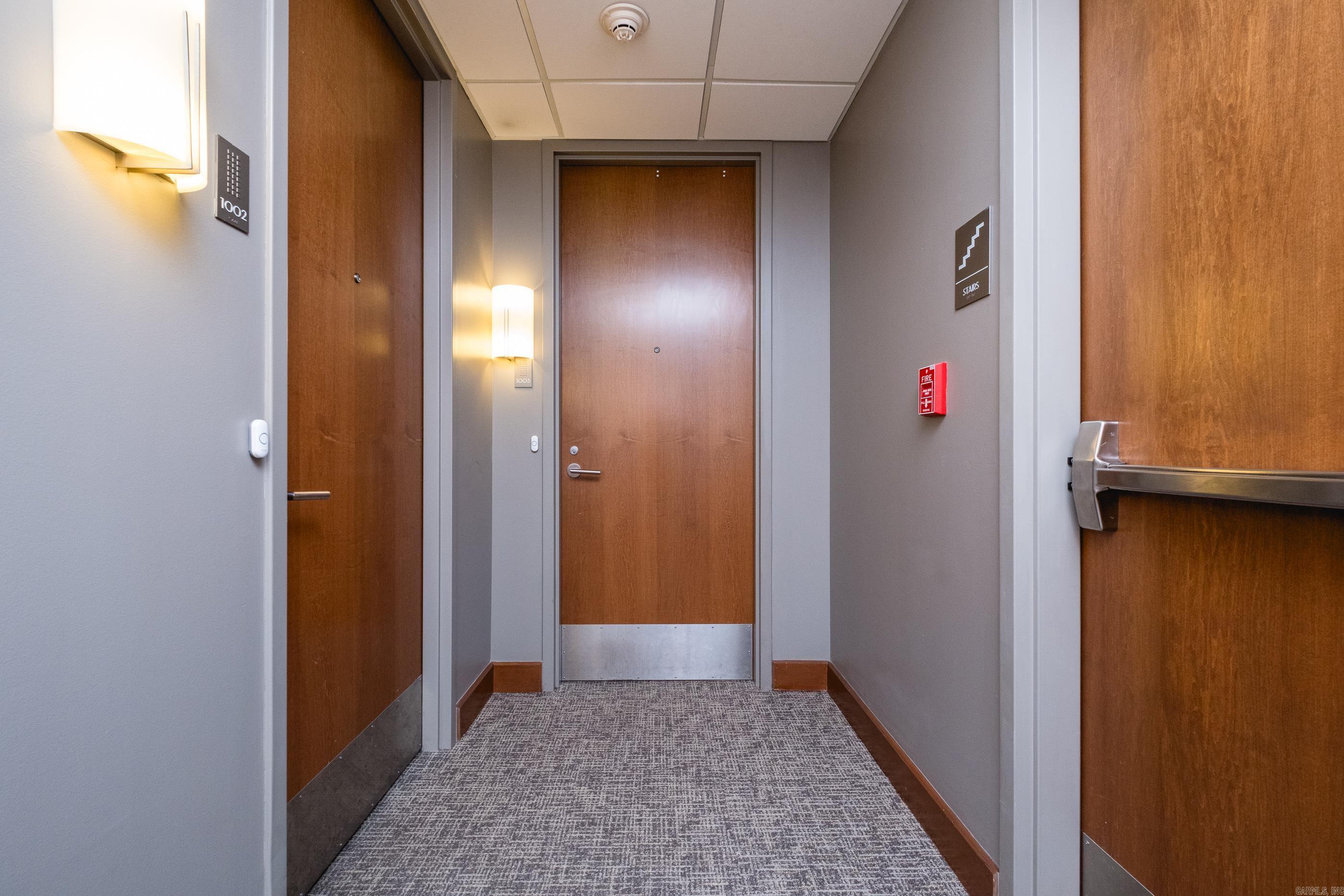 Apartment hallway with wood doors, patterned carpet, and a stairs sign.
