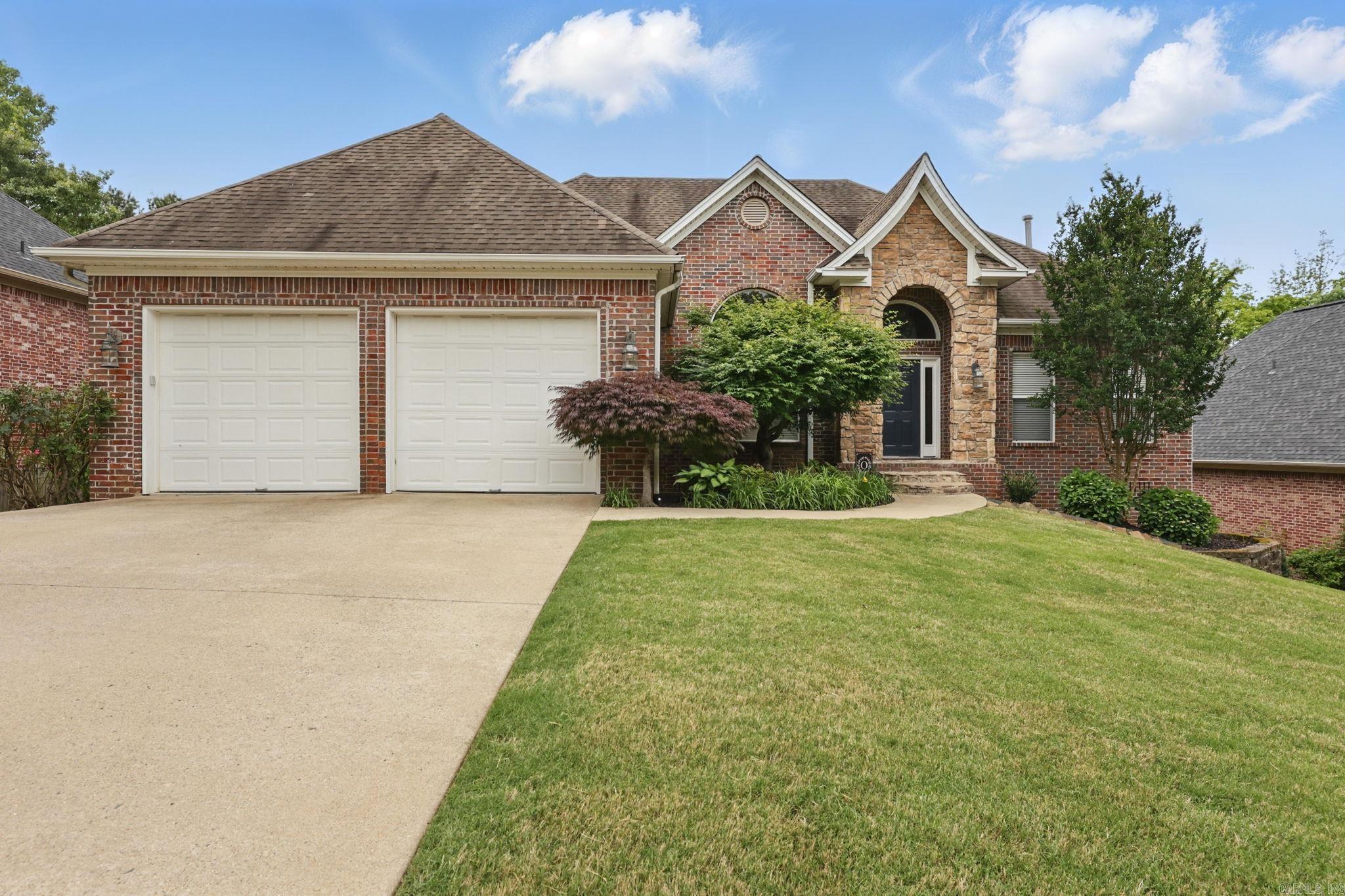 Red-brick house with stone arched entry, double garage, broad driveway, and landscaped lawn.