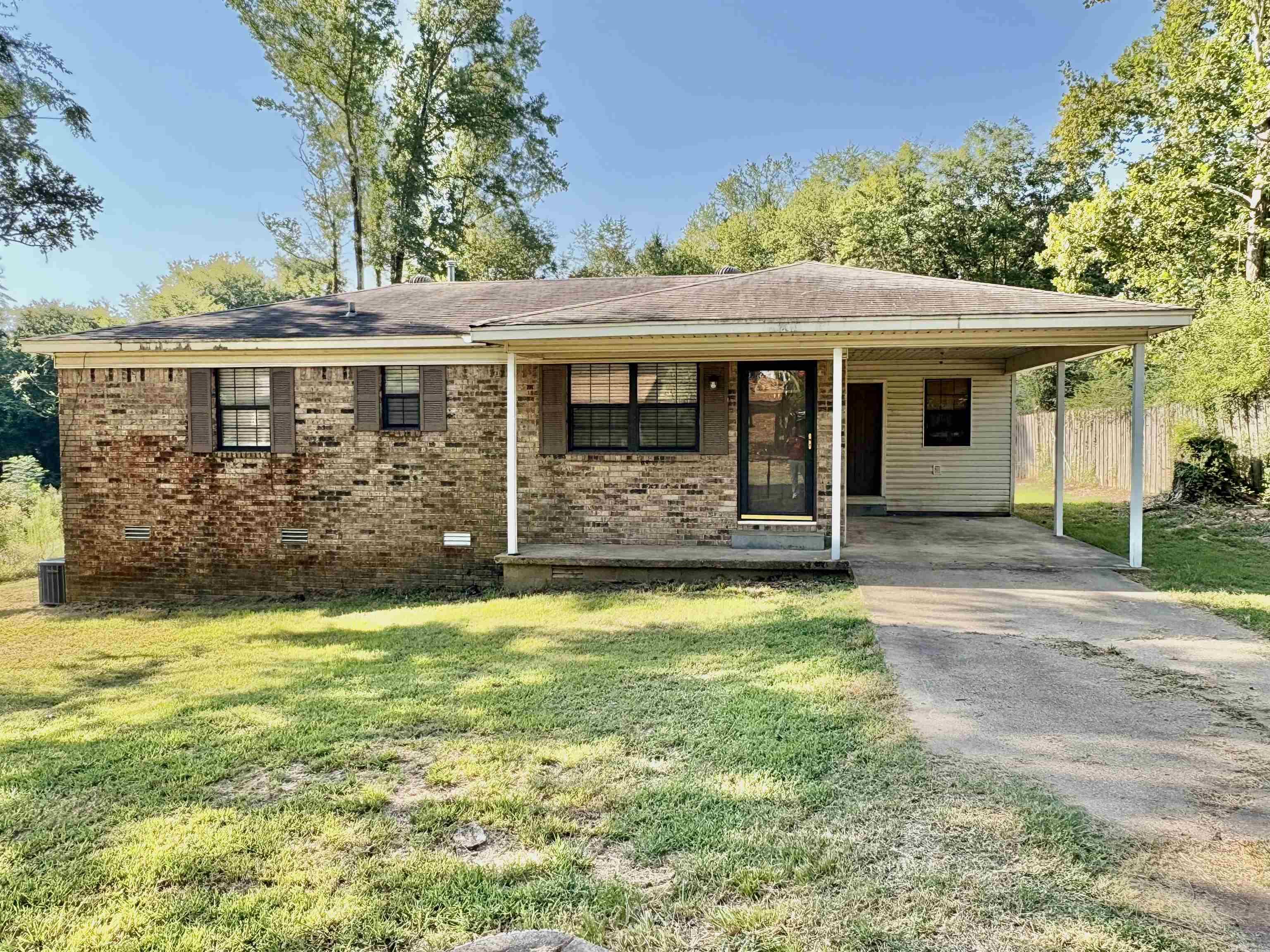 Single-story brick home with a covered porch and attached carport, surrounded by trees.