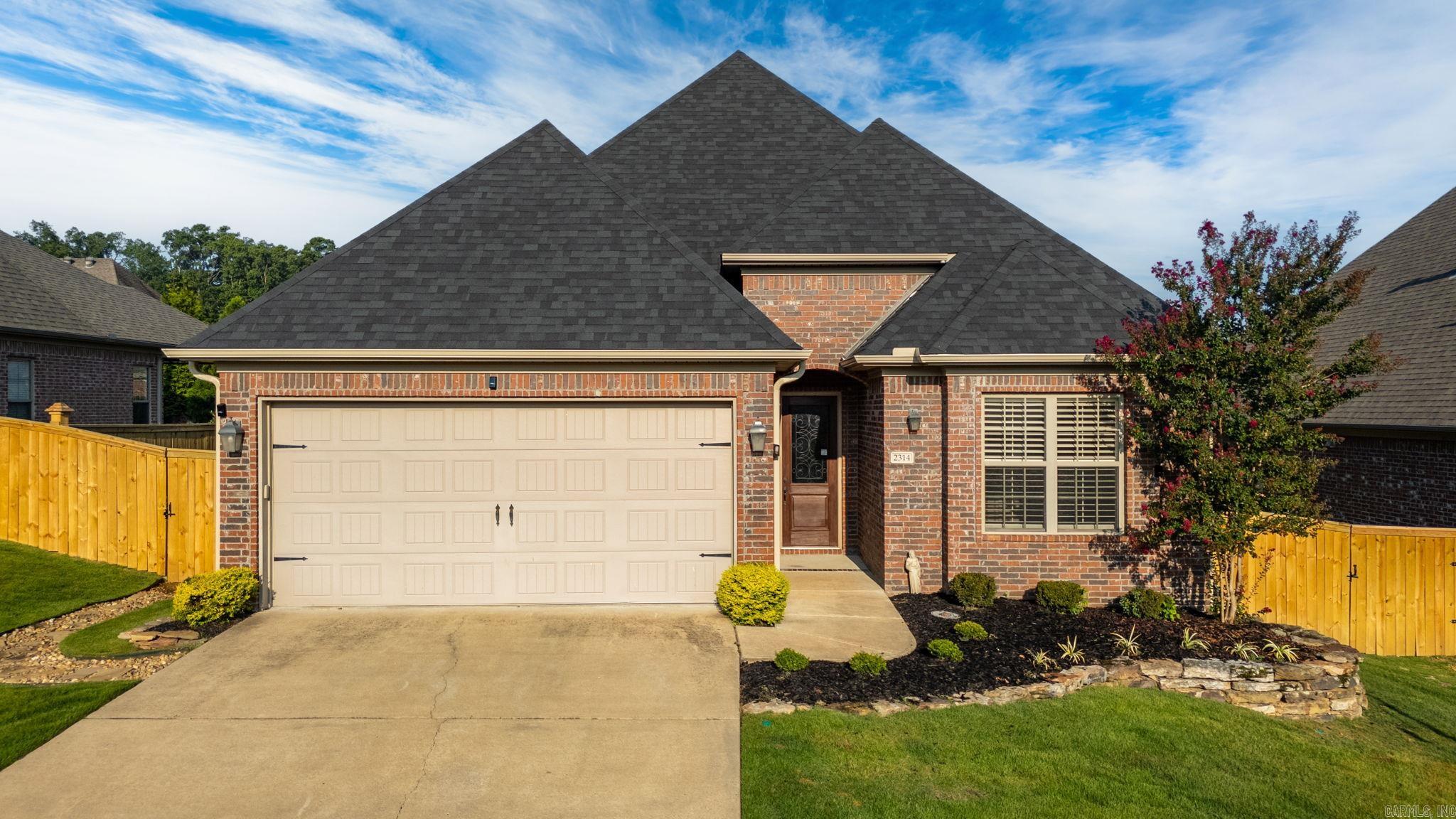 Red-brick house with a multi-gabled roof, two-car garage, landscaped yard, and wooden privacy fencing.