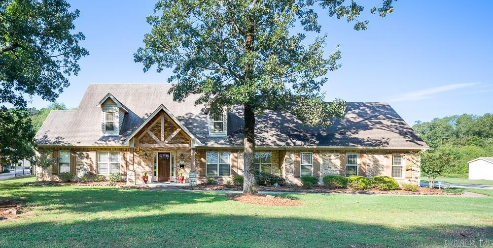 Brick house with gabled roof and dormers, shaded by mature trees across a broad lawn.
