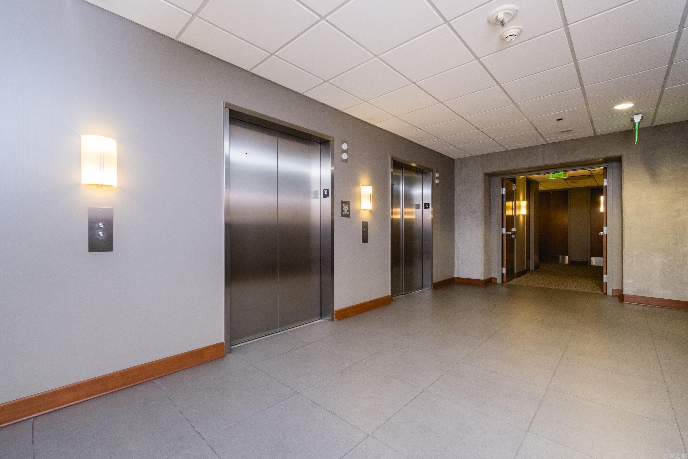 Commercial elevator lobby with two stainless-steel elevators and an open corridor doorway.