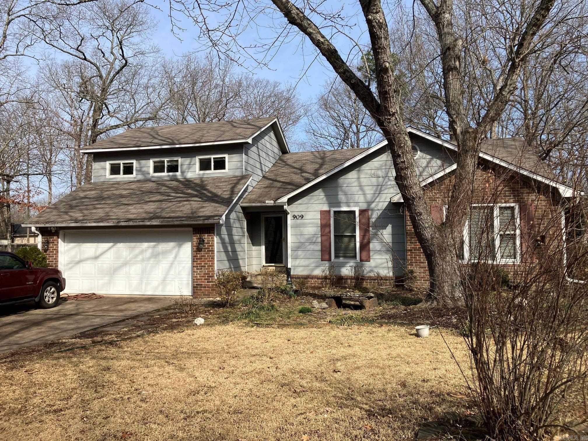 Gray split-level house with brick accents, a two-car garage, and a large leafless tree in front.