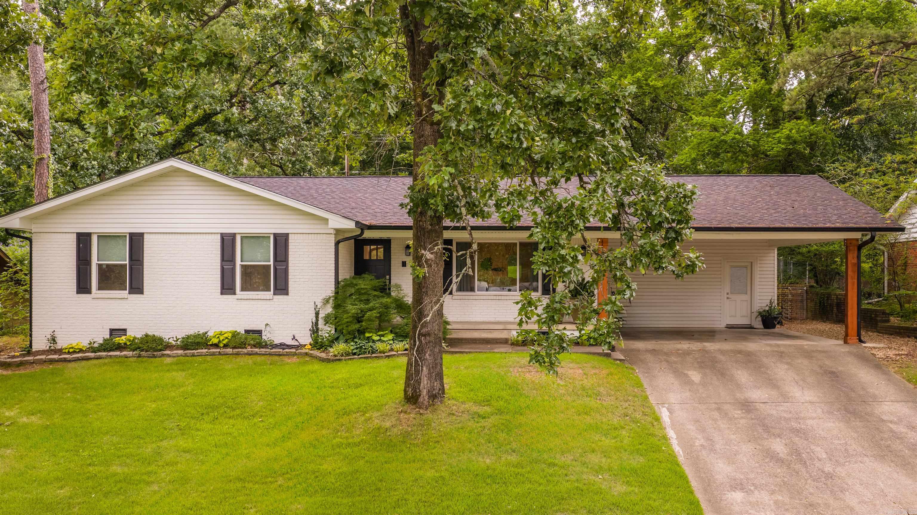 White brick ranch house with a covered carport, driveway, and mature trees.