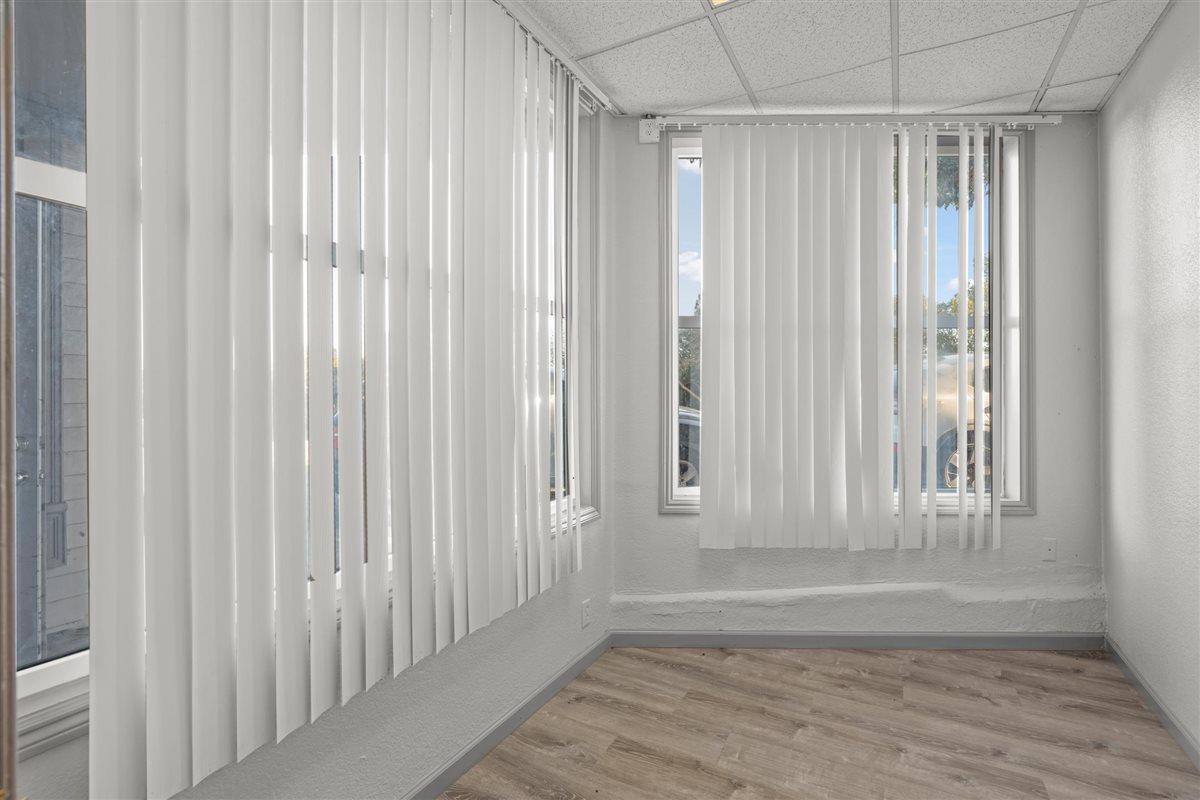 Empty room with wood-look flooring and windows covered by white vertical blinds.