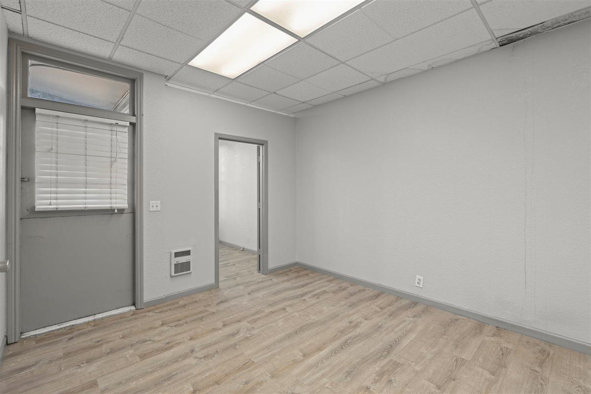 Empty room with light wood-look flooring, a drop ceiling, and a window with blinds.