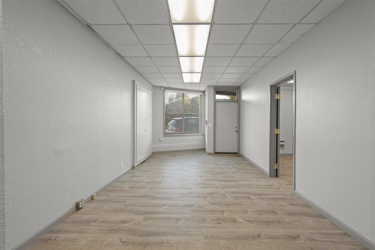 Vacant room with light wood-look floors, a front door, window, and fluorescent ceiling lights.
