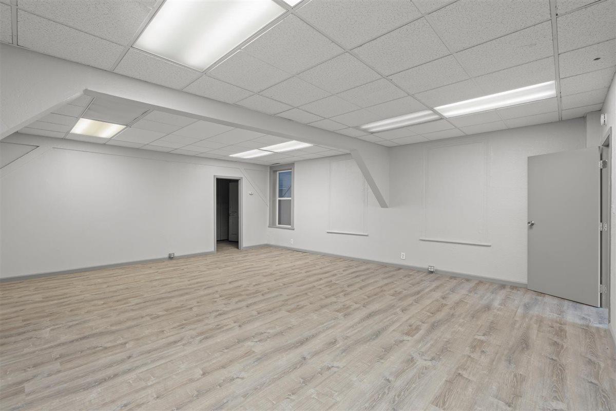 Vacant room with gray wood-look flooring and a suspended ceiling with fluorescent lights.