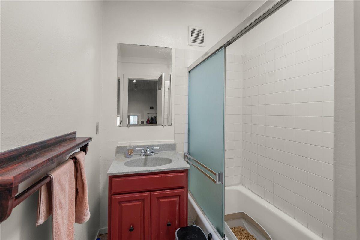 Bathroom with a red vanity and white tiled tub behind a blue-green frosted shower door.