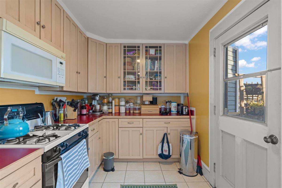 Kitchen with pale wood cabinets, red countertops, and a gas range beside a glazed door.