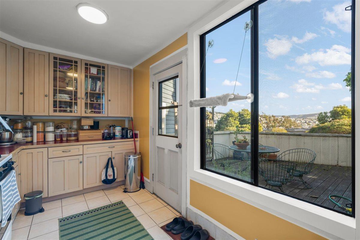 Kitchen with light wood cabinets and a window overlooking a deck and hillside homes.