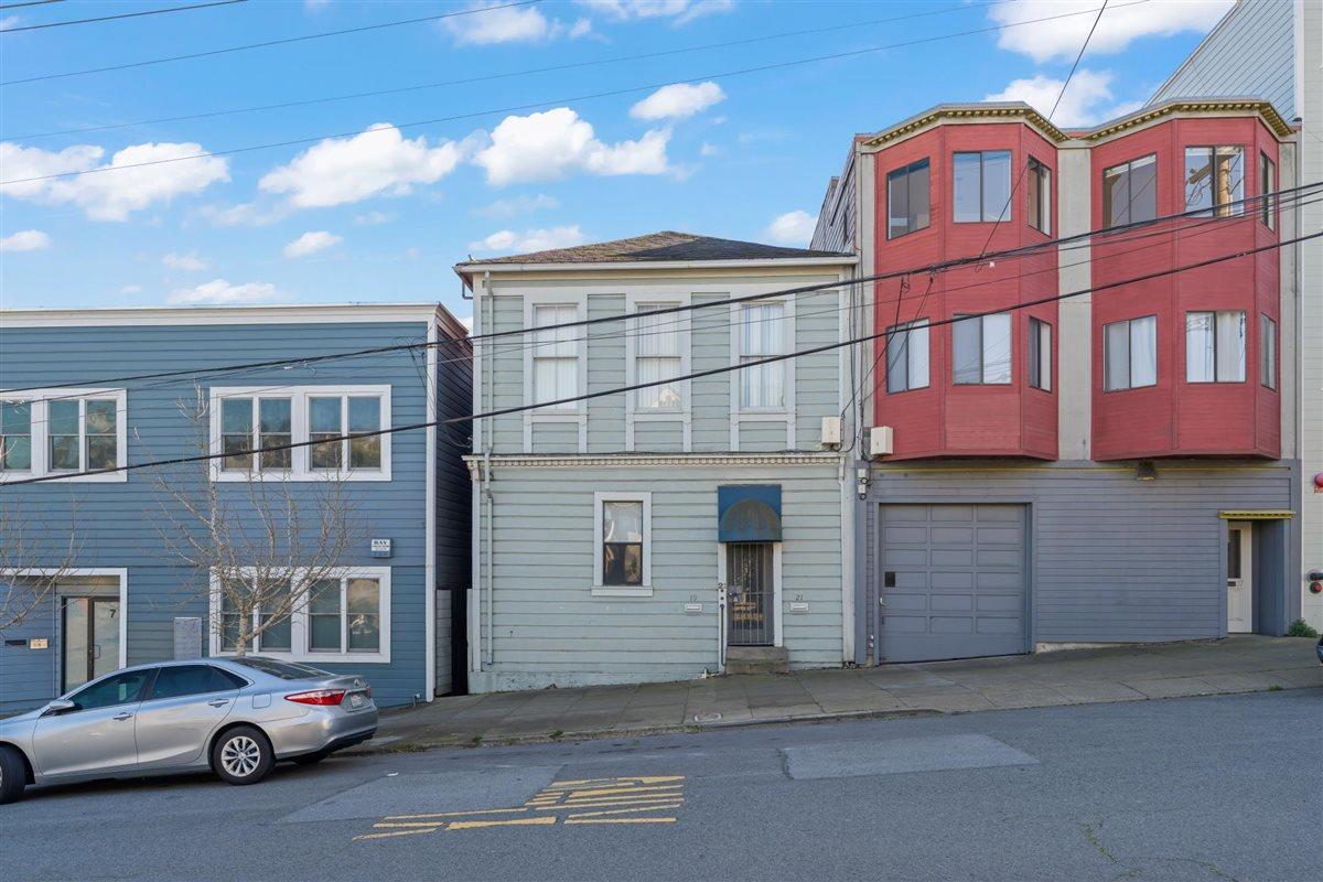 Pale green San Francisco home with a blue entry awning beside a red bay-windowed building.