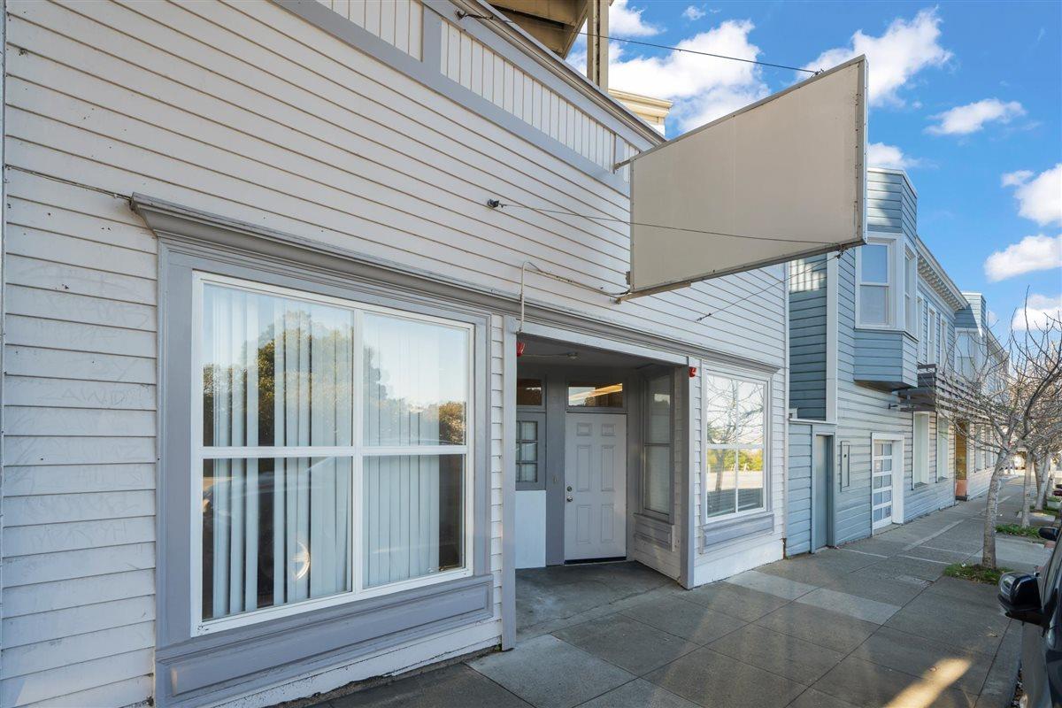Light gray building exterior with large windows, a recessed entrance, and a projecting blank sign panel.