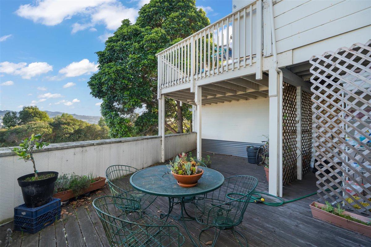 Wooden patio with round metal table, potted plants, and elevated white deck overlooking trees and distant hills.