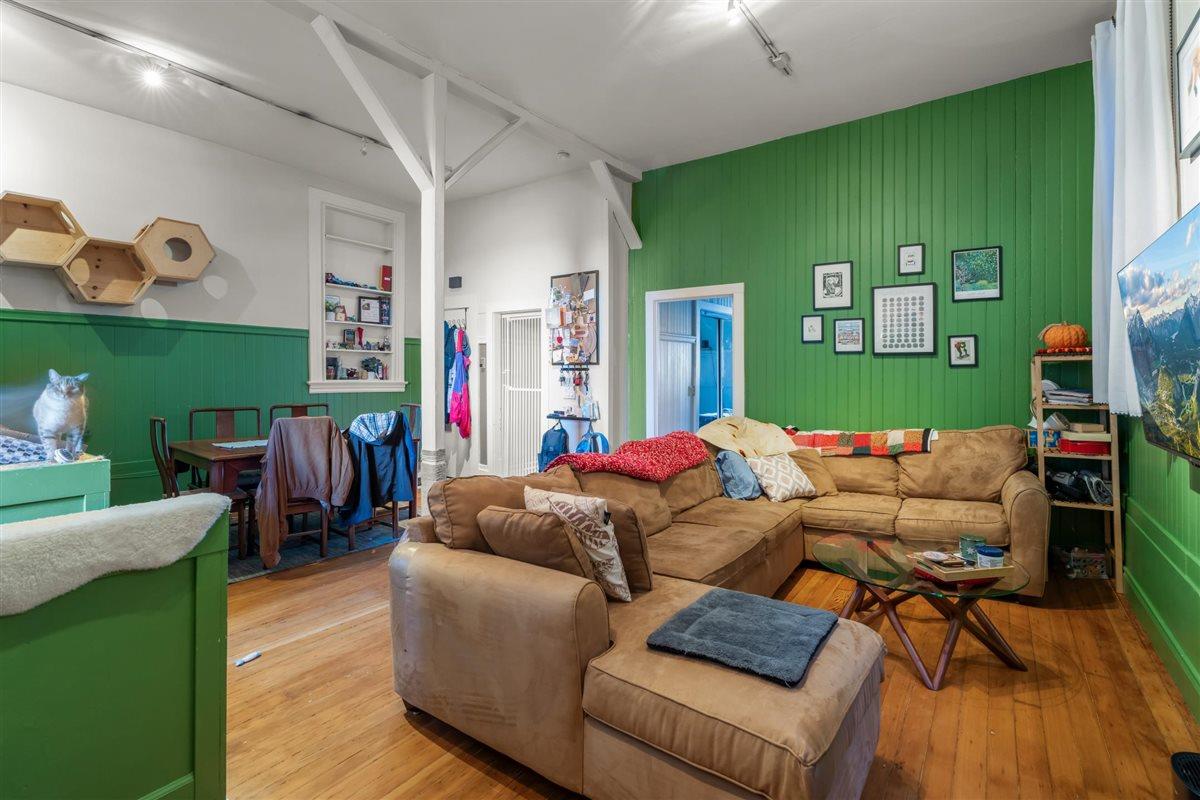 Living room with green paneled walls, a tan sectional, hardwood floors, and a cat on a cabinet.