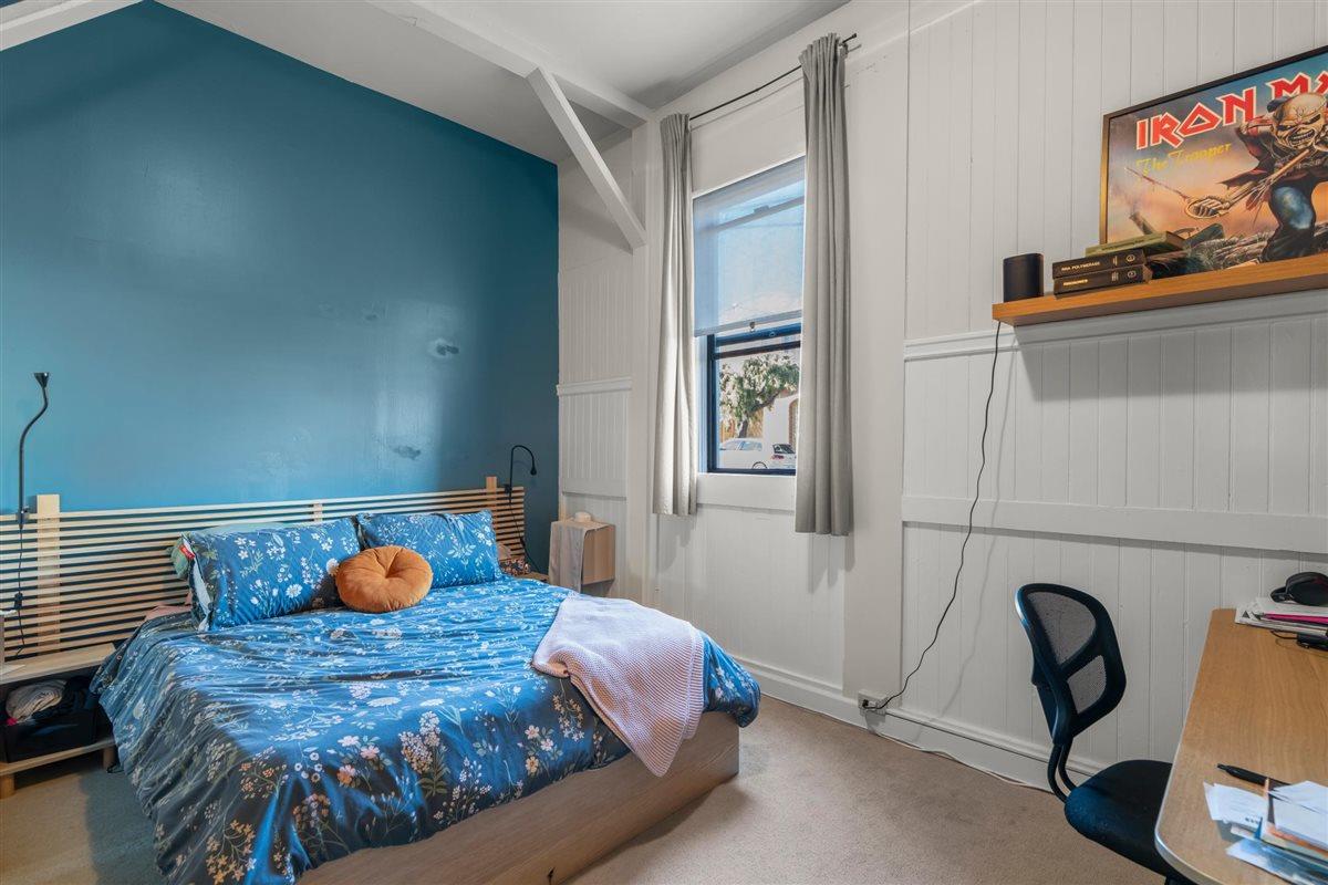 Bedroom with blue floral bedding, a teal accent wall, white paneling, and a desk.