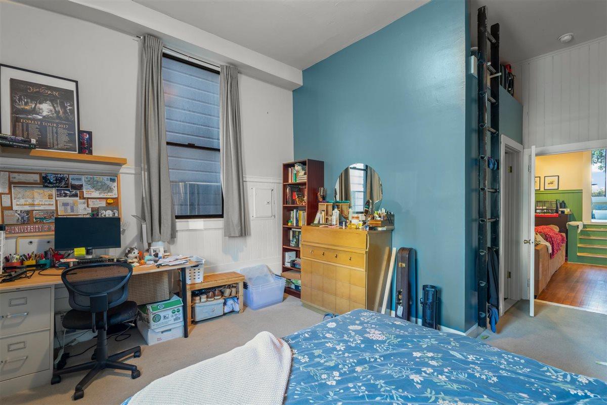 Bedroom with a blue accent wall, desk beneath a window, and climbing wall.