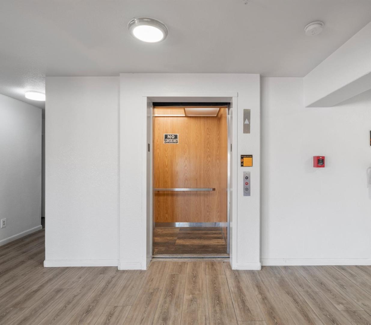 Elevator lobby with an open, wood-paneled elevator and wood-look flooring.