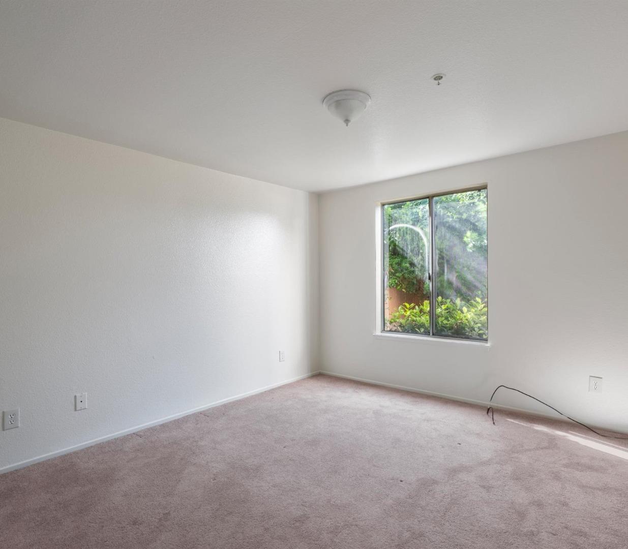 Empty carpeted bedroom with a large window overlooking greenery.