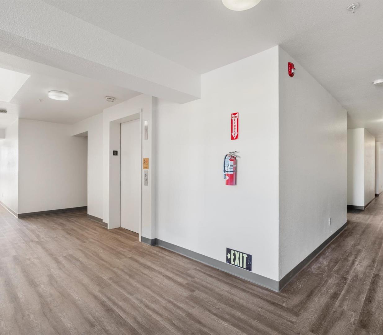 Building hallway with an elevator, wood-look flooring, and a wall-mounted fire extinguisher.