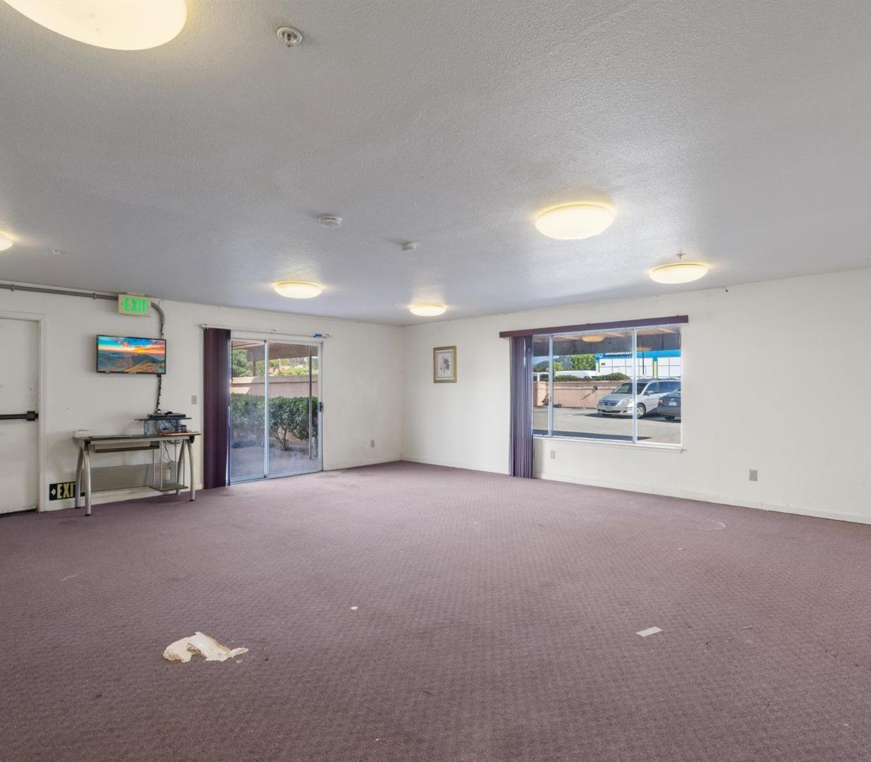 Mostly empty carpeted room with sliding glass doors, a wide window, ceiling lights and an exit door.