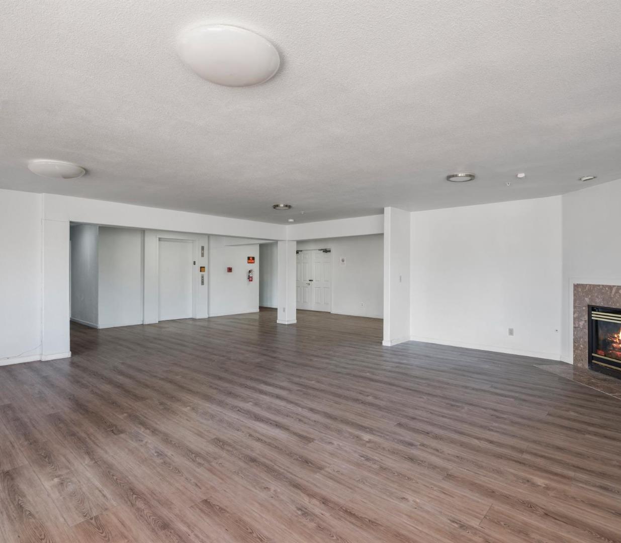 Empty multifamily common area with gray wood-look flooring, an elevator, and a fireplace.
