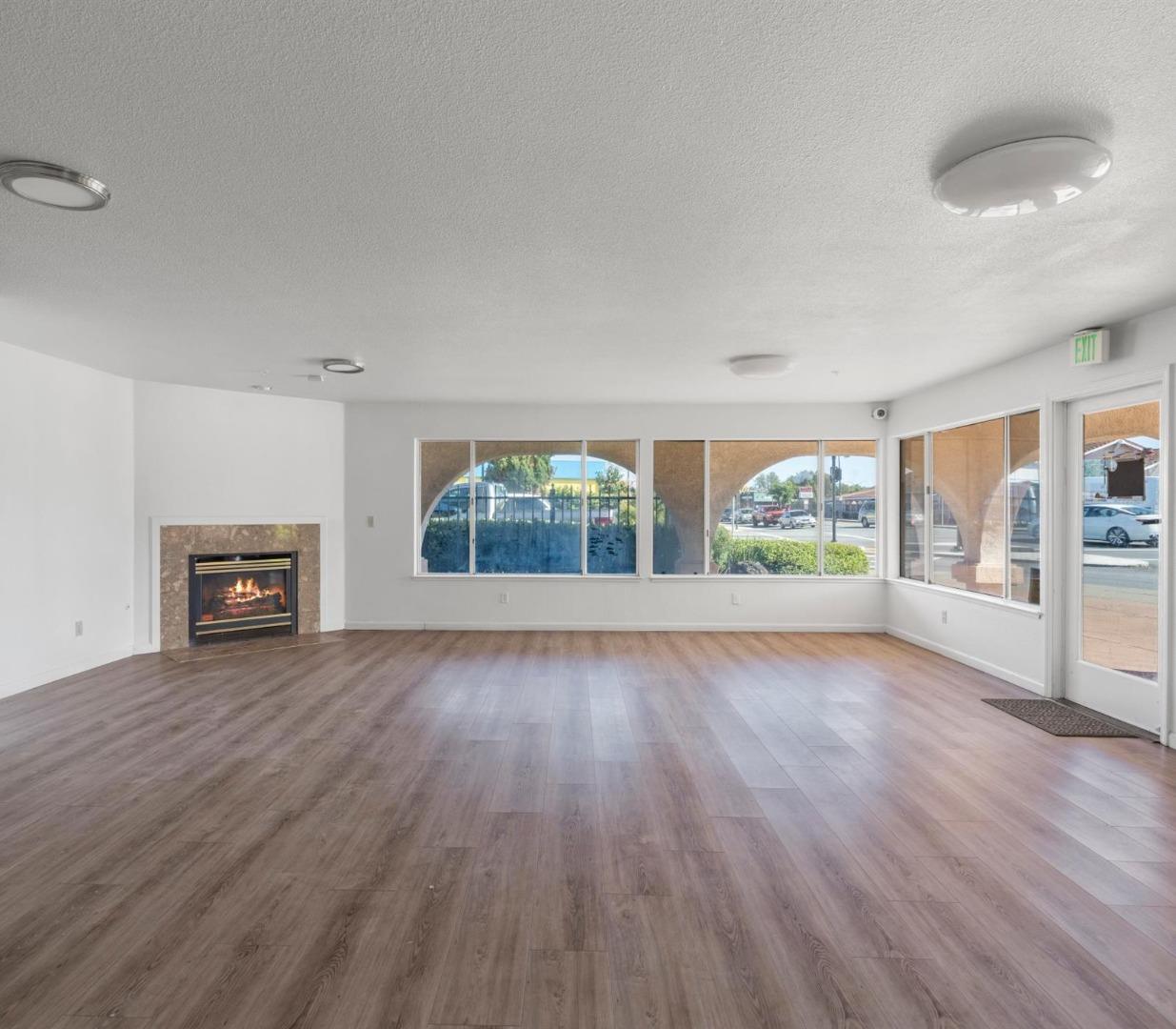 Vacant open interior with wood-look flooring, a fireplace, and large street-facing windows.