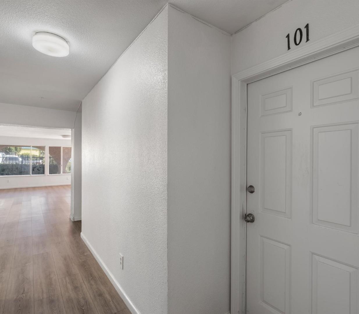 Apartment entry hallway with door 101 and wood-look flooring leading to a bright living area.