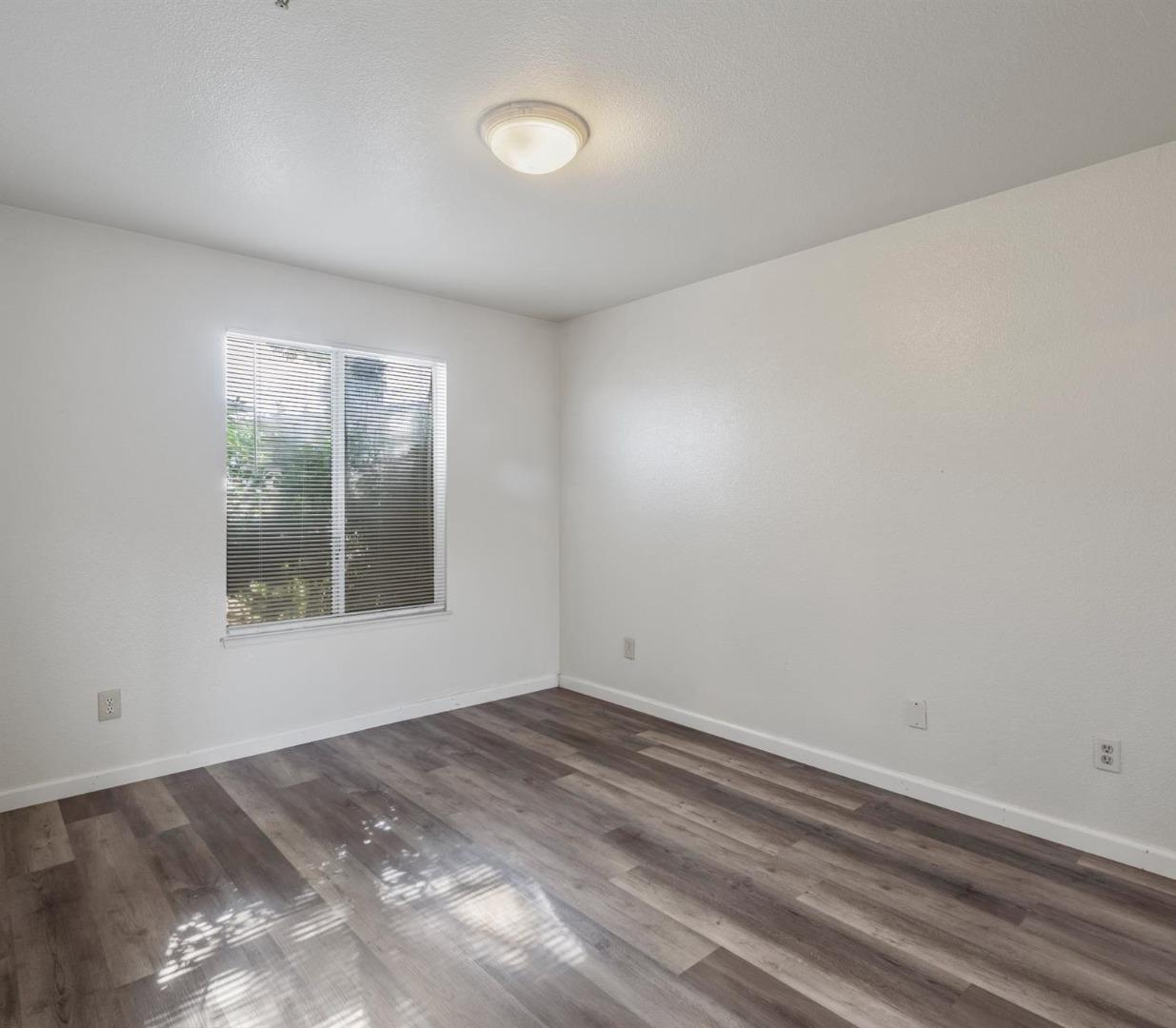 Empty room with gray wood-look flooring, a window with blinds, and sunlight on the floor.