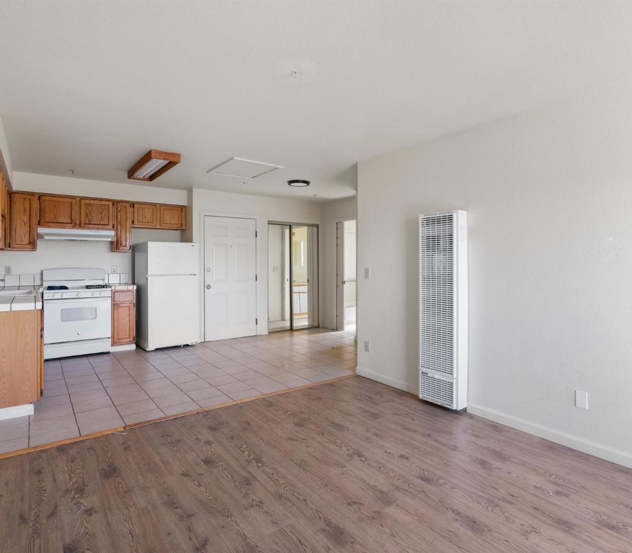 Open-plan apartment kitchen and living area with wood cabinets, white appliances, and wood-look flooring.