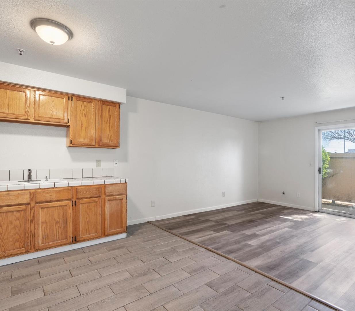Vacant kitchen and living area with oak cabinets, tiled counter, and sliding glass door.