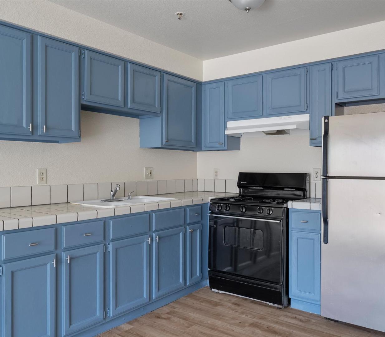 Kitchen with blue cabinets, tiled counters, a black range, and stainless steel refrigerator.