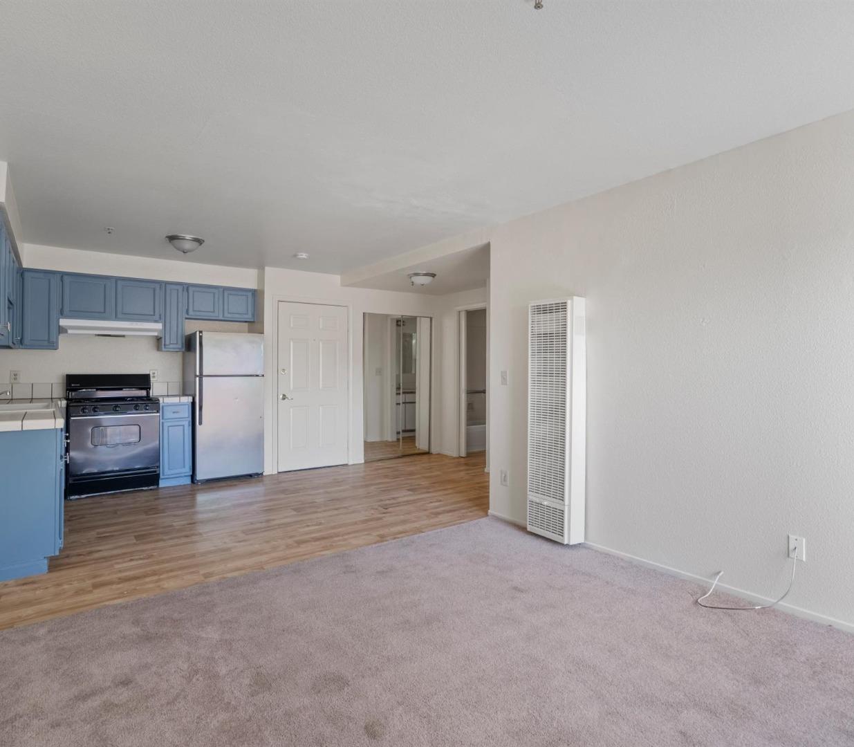 Unfurnished living area with carpet beside an open kitchen with blue cabinets and wood-look flooring.