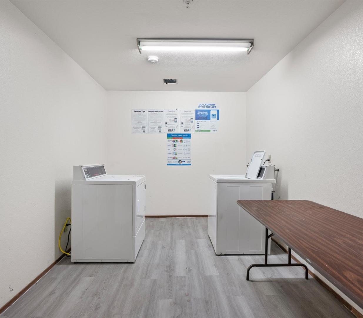 Laundry room with two commercial machines, a folding table, and instructional signs.