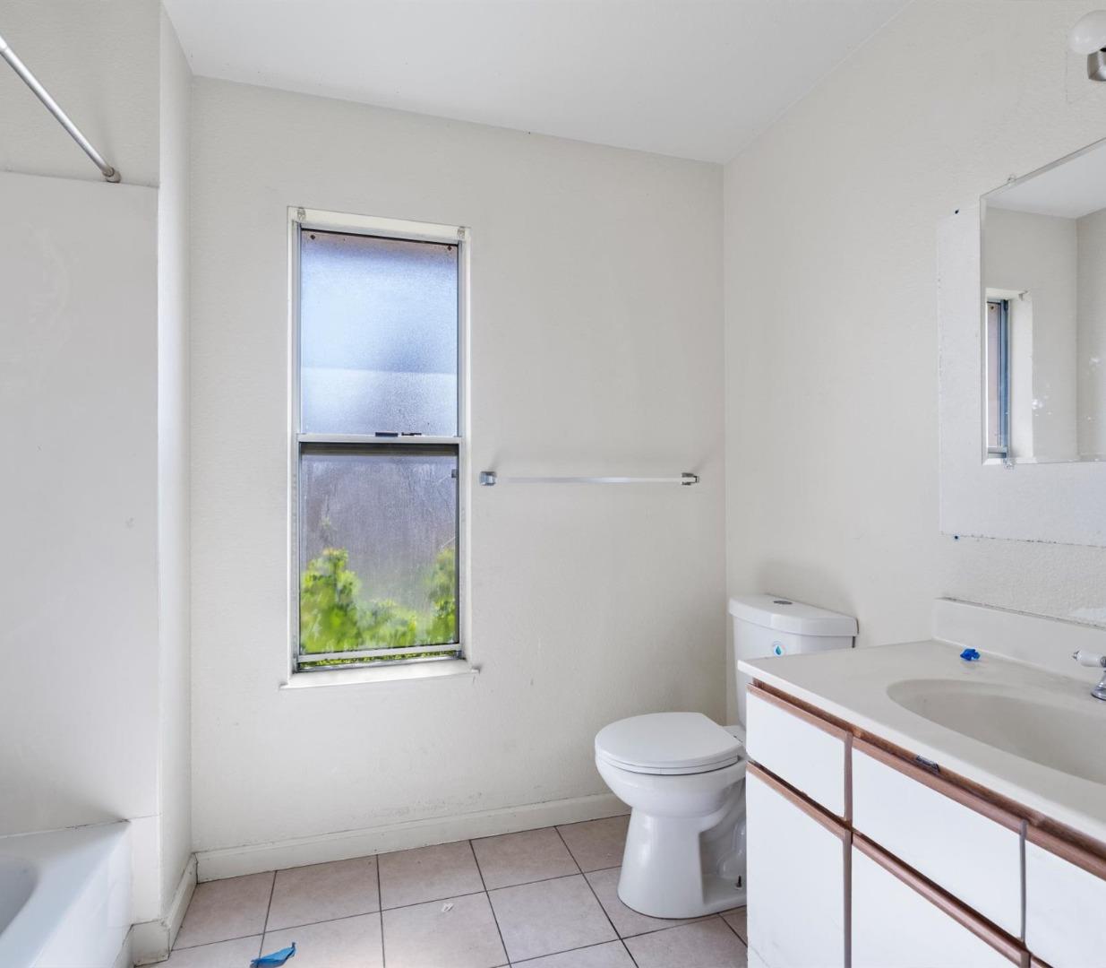 Bathroom with a large window, bathtub, toilet, and white vanity.