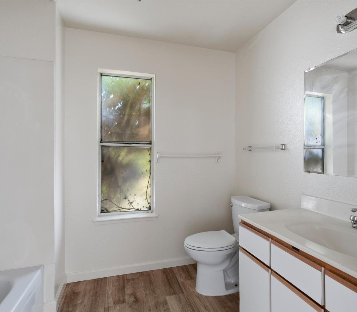 Empty bathroom with a narrow window, white fixtures, wood-trimmed vanity, and wood-look flooring.
